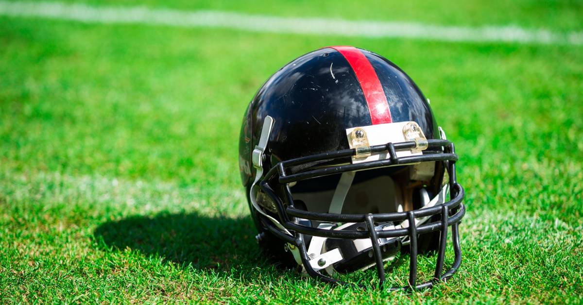 A black football helmet with a red stripe decal across the crown resting on an American football field.